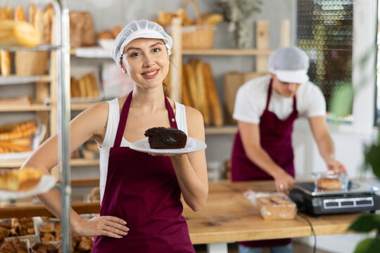 Polite young female seller offering pie piece in disposable plate in bakeshop
