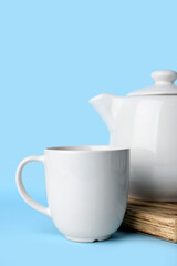 White ceramic empty mug and tea pot on board on blue background