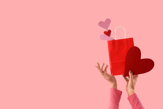 Woman holding gift bag with hearts on pink background. Valentine's Day celebration