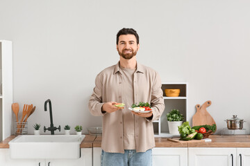 Handsome man holding plate with boiled eggs, avocado toast and vegetables in kitchen