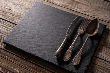Retro metal cutlery on granite surface over aged wooden background. Vintage cutlery on granite...