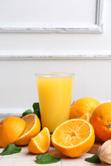 Glass of tasty juice with oranges and mint leaves on white tile table