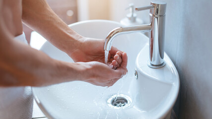 A person is washing their hands at a sleek bathroom sink. Water flows from the chrome faucet into the basin. Sunlight brightens the scene, creating a calm atmosphere.