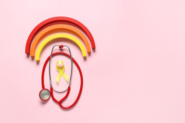 Obraz premium Yellow ribbon, toy rainbow and stethoscope on pink background. Childhood cancer awareness concept