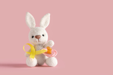 Toy bunny, pacifier and yellow ribbon on pink background. Childhood cancer awareness concept