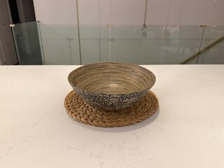 Woven Home Decor: Handmade natural fiber bowl and placemat arranged on a sleek white countertop in a minimalist modern kitchen.