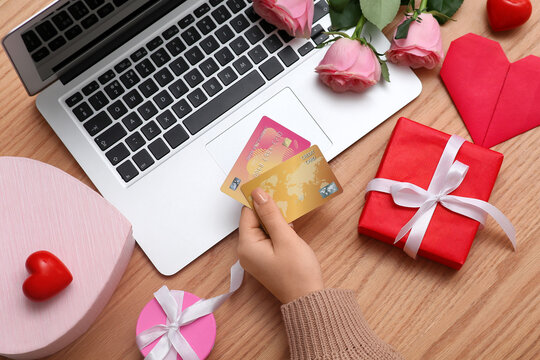 Female hands with credit cards, pink roses, gift boxes and modern laptop on wooden background. Valentine's Day celebration - Powered by Adobe