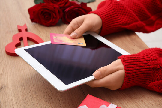 Female hands with credit card, modern tablet computer and red roses on wooden table. Valentine's Day celebration
