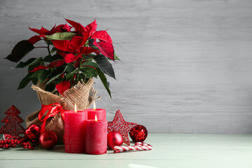 Beautiful Christmas plant poinsettia, decorations and burning candles on light wooden table
