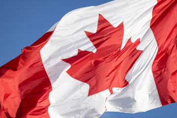 Fototapeta premium Red and white Canadian flag with a maple leaf waving in the air in downtown Toronto near Ontario Lake. Canadian patriotism and culture