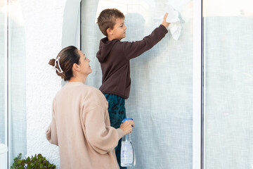 Mother and son cleaning windows together in their cozy home, enjoying family time and building a strong bond during chores