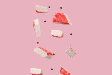 Cut tasty crab stick and peppercorns flying on pink background