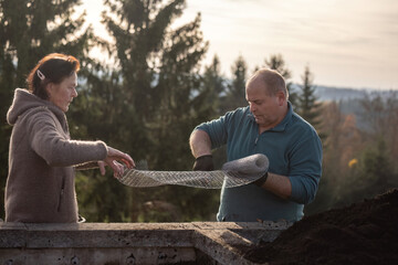 Man and woman working together outdoors with wire mesh during a manual task in autumn