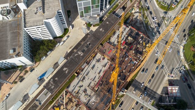 Aerial view of road construction site with working cranes next to moving railway system and highway on a sunny day