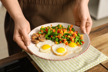 Woman preparing tasty dinner with fried quail eggs and mix of vegetables in kitchen, closeup