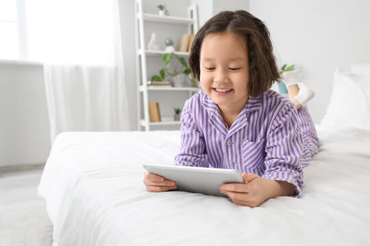 Little Asian girl watching cartoons on tablet computer in bedroom - Powered by Adobe