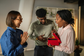 Diverse coworkers celebrating and exchanging gift in office