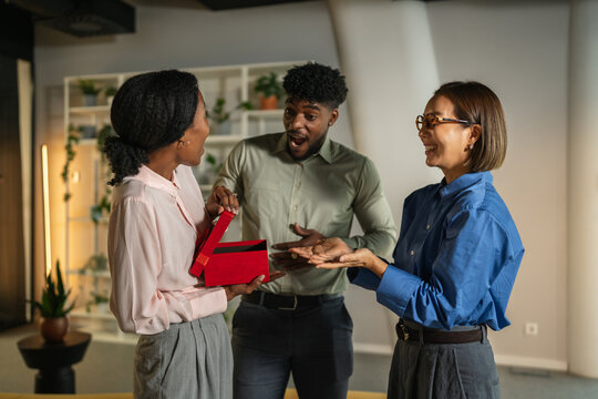 Diverse coworkers celebrating and exchanging gift in office