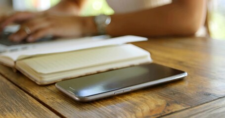 Lying smartphone at right front on wooden table at home, with notebook laptop watch sleeveless top