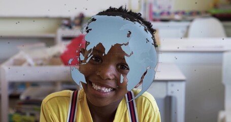 Smiling boy sitting at school desk wearing yellow top and striped suspenders, showing globe overlay