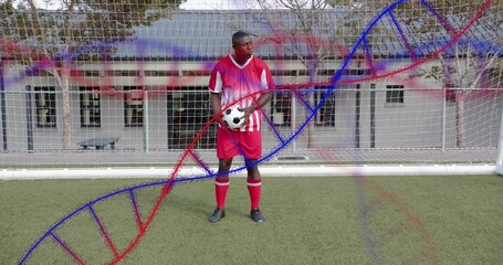 Standing soccer player wearing red-and-white holding ball on turf with goal net helix overlay