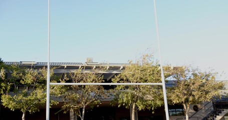 Framing pair of tall white goalposts dominating stadium exterior, showing covered stands