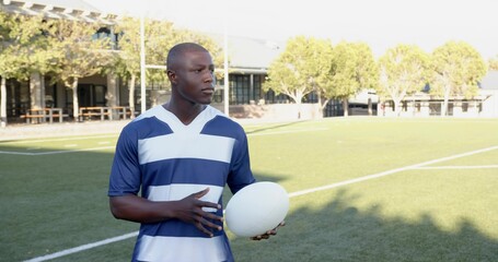 Holding white oval ball, athlete standing on marked grass sports field, wearing striped jersey