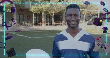Smiling man wearing blue jersey holding white ball on sports turf, with neon gaming icons