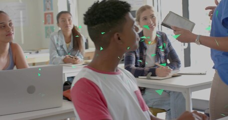 Sitting teenage boy in white shirt red sleeves facing teacher in classroom, teacher holding tablet