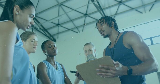 Talking coach in dark tank holding clipboard at gym with players in light-blue jerseys, copy space