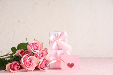 Pink roses with gift boxes and letter on table against white background. Valentine's Day celebration