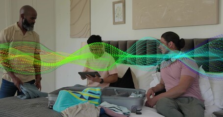 Packing three men arranging casual clothes on bed at home, with open suitcase, tablet, digital wave