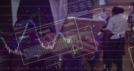 Holding tablet, man wearing dark blazer, light shirt viewing stock charts at expo with keyboard
