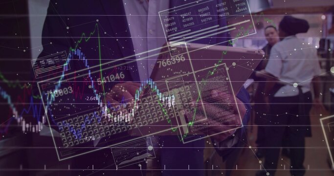 Holding tablet, man wearing dark blazer, light shirt viewing stock charts at expo with keyboard