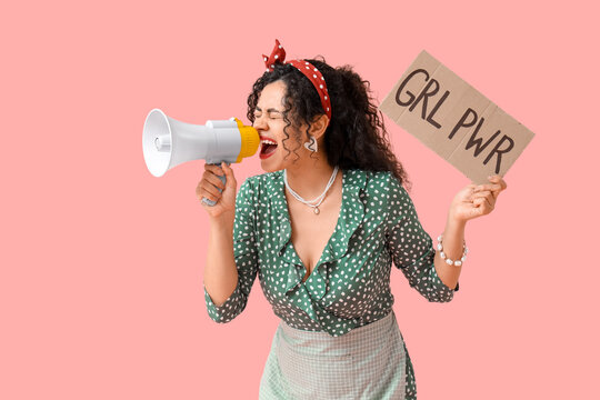 Young African-American pin-up woman with GRL PWR sign shouting into megaphone on pink background. Women's History Month