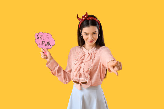 Young pin-up woman with GRL PWR sign pointing at viewer on yellow background. Women's History Month