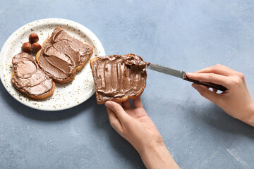 Young woman preparing tasty toasts with chocolate spread and hazelnuts on blue grunge background