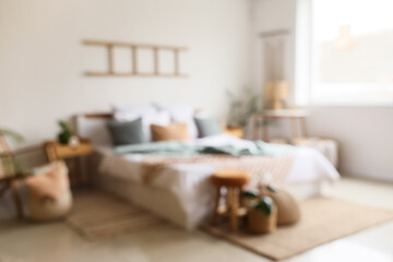 Blurred view of light bedroom with big bed and tables
