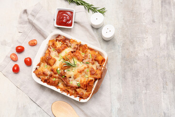 Baking dish with tasty pasta, rosemary, cut green onion, tomatoes and bowl of ketchup on light grunge background