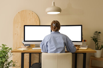 Young woman working with computer at table in office, back view