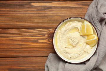 Bowl of delicious hummus with lemon on wooden background