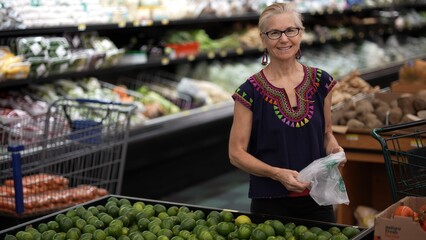 Portrait of pretty smiling mature woman choosing limes in a grocery store wearing ethnic clothes.
