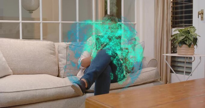 Man tapping tablet at home, creating teal hologram globe expanding, rotating, exploring tech data