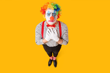 Young man dressed as sad pantomimist on yellow background, top view. April Fool's day celebration