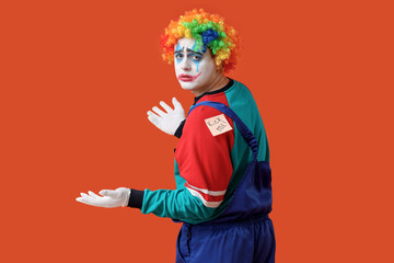 Sticky note with text KICK ME on back of young man dressed as sad clown against orange  background. April Fool's Day celebration