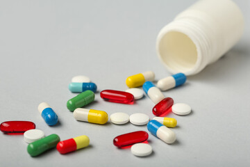 Bottle with different scattered pills on grey background, closeup