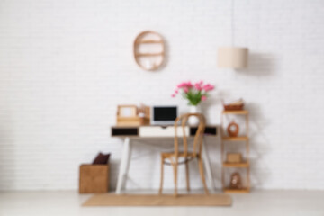 Blurred view of stylish workspace with modern laptop, beautiful tulip flowers and shelving unit near white brick wall