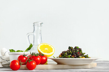 Plate with healthy quinoa salad and ingredients on marble table near white wall