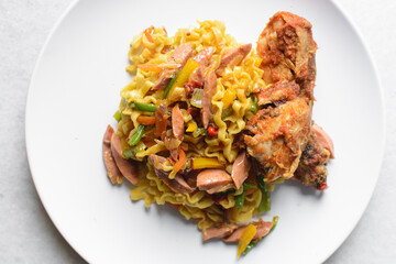 Overhead view of egg noodles with peppers, sausage and peppered chicken on a white plate, top view of egg noodles with spicy chicken