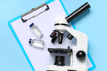 Modern microscope with clipboard and ampoules on blue background